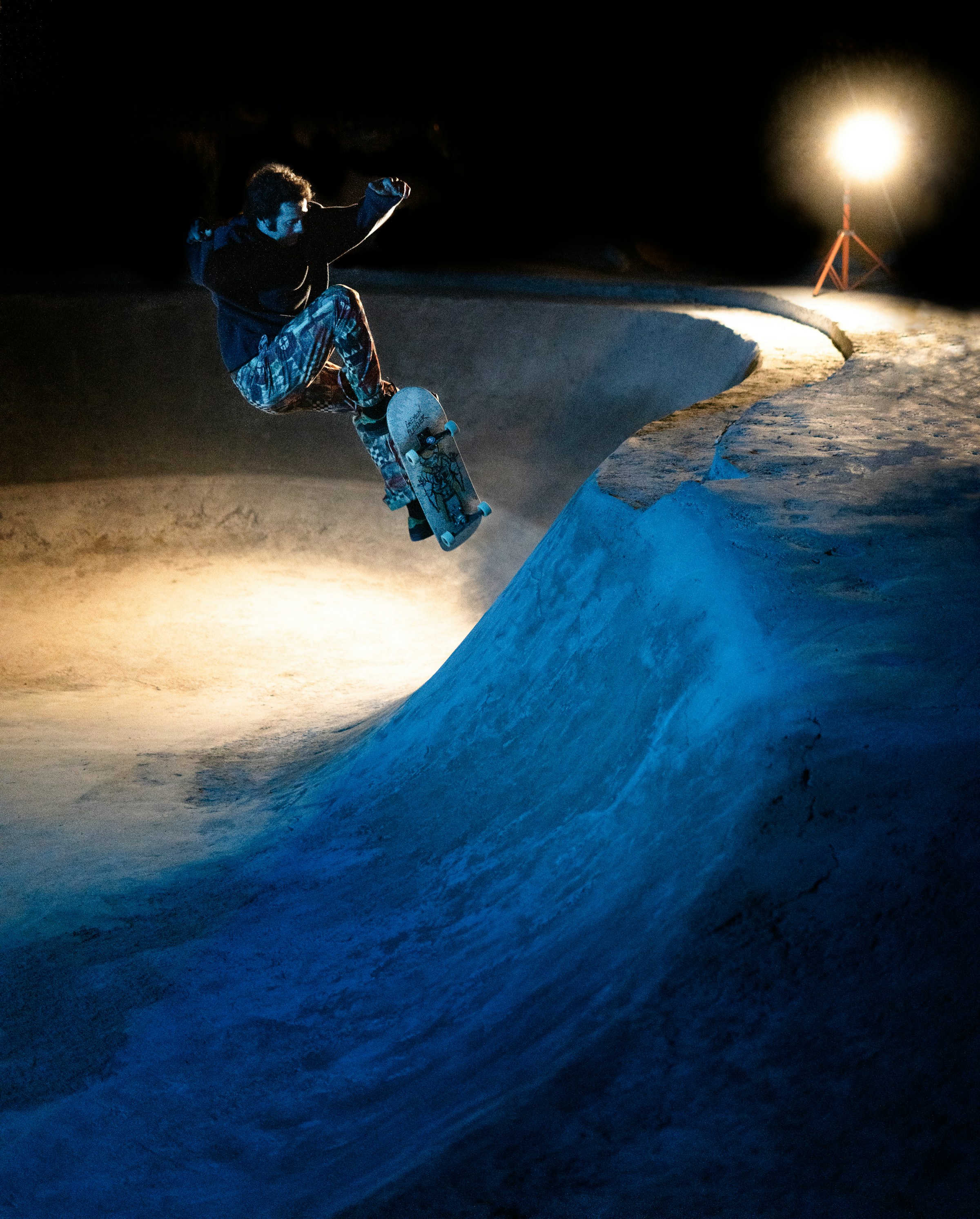 A skateboarder flying above a concrete bowl at night